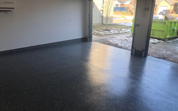 Dark gray textured flake floor at an open garage door with snow outside