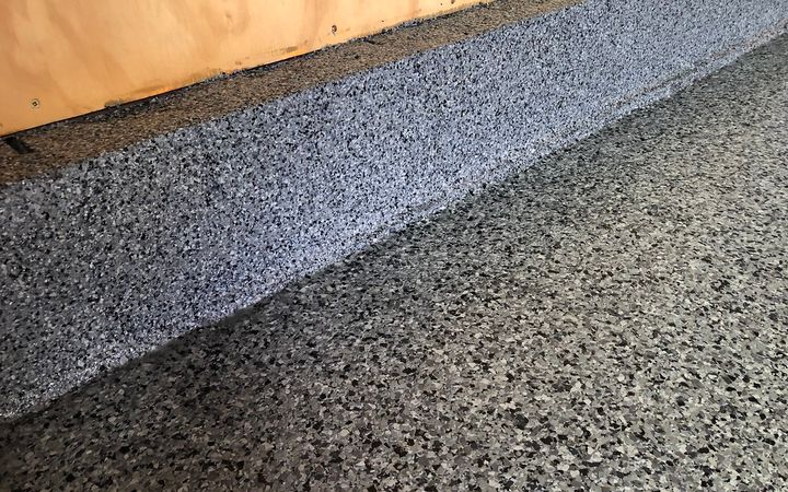 Close view of a gray and black flake floor running over a step