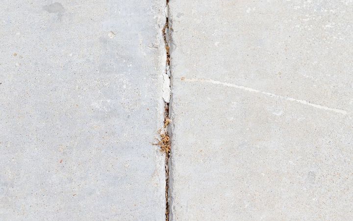 Crack running beside a saw-cut joint in a gray concrete slab