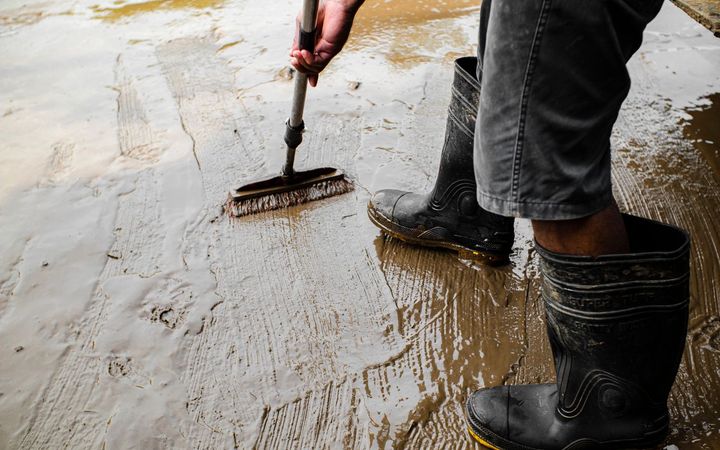 Worker in rubber boots brushing a primer coat across a concrete floor