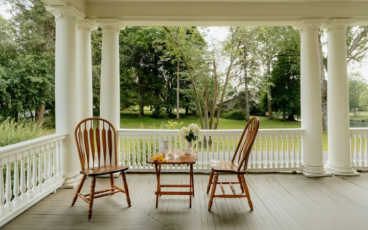 Covered front porch with white columns, two wooden chairs and a small table